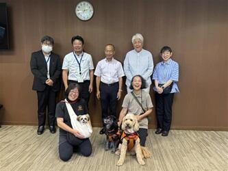 学長室で本学教員と日本聴導犬協会スタッフと補助犬３頭の集合写真