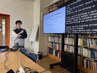 スウェーデン王立工科大学で講演を行っている。大きな本棚の前にモニターがあり、資料を写しながら話している様子。