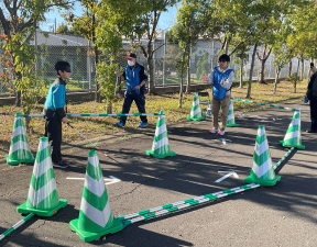 一般の方がアイマスクを付けて、カラーコーンで作られたコースを白杖を使って歩く様子