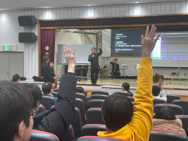 バイオリンの値段当てクイズで、一番高いバイオリンを挙手によって回答する様子