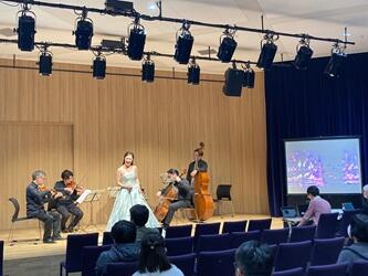ステージ上に左からヴァイオリン、ヴィオラ、チェロ、コントラバス、中央にソプラノ歌手が演奏している様子。右端のスクリーンで指紋を表示